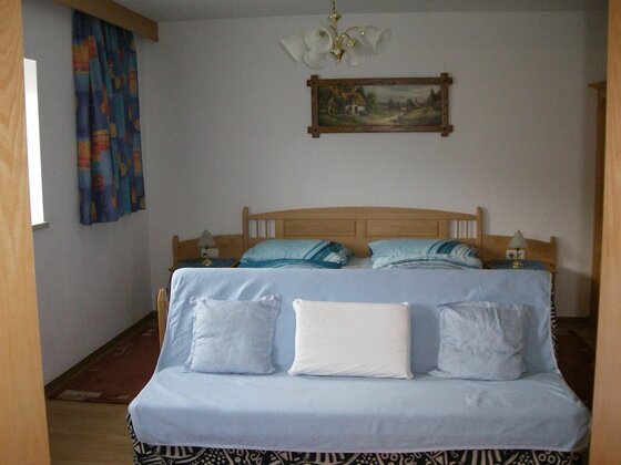 Schlafzimmer mit Doppelbett aus Holz und davorstehendem hellblauem Sofa mit Kissen.