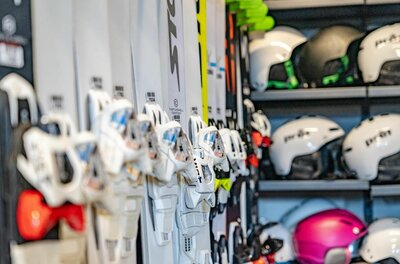 Nahaufnahme von aufgereihten Skiern mit Bindungen und Skihelmen in einem Regal.