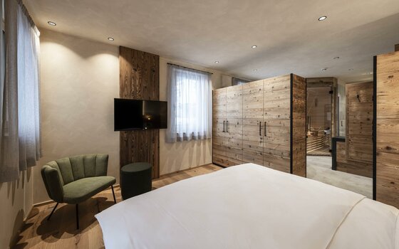 Modernes Schlafzimmer mit Doppelbett, Holzschrank, grünem Sessel und TV an der Wand.