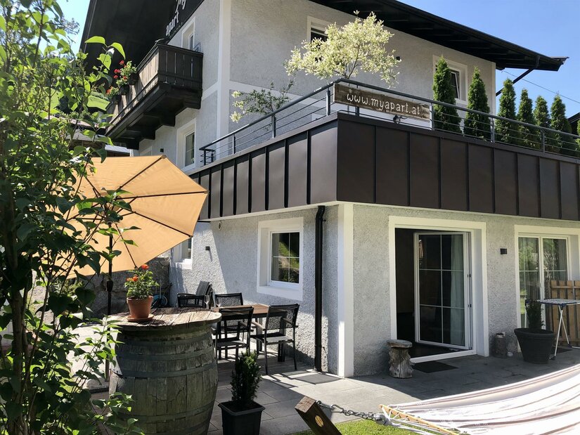 Außenansicht eines Ferienhauses mit Terrasse, Sonnenschirm, Sitzgruppe und großem Balkon.