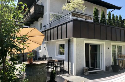 Außenansicht eines Ferienhauses mit Terrasse, Sonnenschirm, Sitzgruppe und großem Balkon.