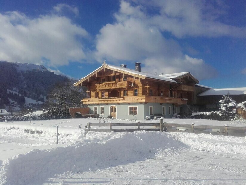 Fichterhof Kitzbühel im Winter Ein traditionelles Holzhaus mit Balkonen in einer verschneiten Winterlandschaft vor Bergen.