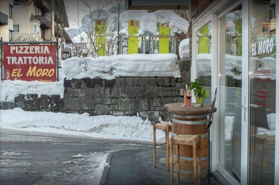 El Moro Winter Außenansicht der Pizzeria El Moro im Winter mit einem Weinfass-Stehtisch vor dem Eingang.