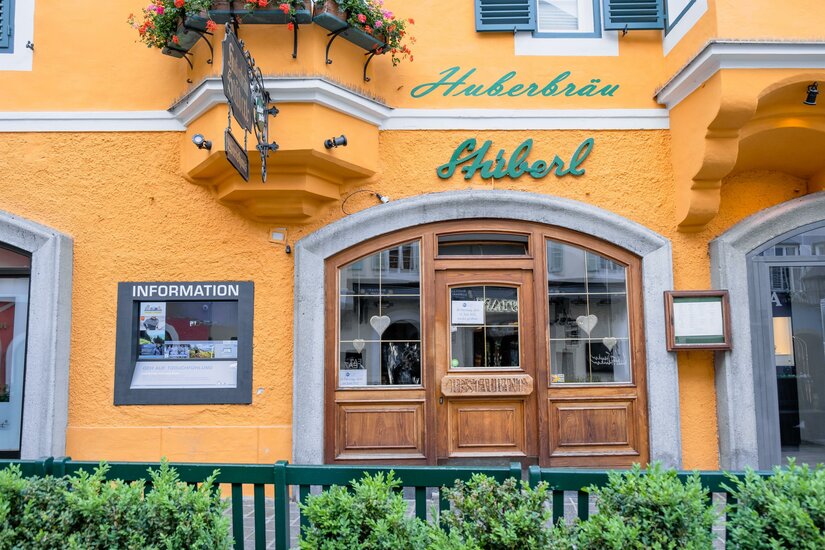Ein einladendes Restaurant mit einer hellgelben Fassade und grünen Akzenten. Die Fenster sind mit Blumenkästen geschmückt.