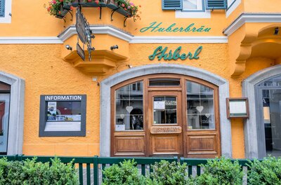 Huberbräu Ein einladendes Restaurant mit einer hellgelben Fassade und grünen Akzenten. Die Fenster sind mit Blumenkästen geschmückt.