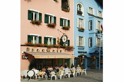 Café Praxmair in Kitzbühel Außenansicht eines Cafés mit Gästen an Tischen vor einer rosa und blauen Hausfassade.