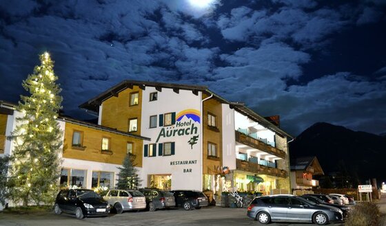 Hotel Aurach bei Nacht Beleuchtetes Hotel Aurach bei Nacht mit Parkplatz und geschmücktem Weihnachtsbaum.