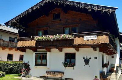 Zweistöckiges alpines Haus mit dunkler Holzfassade im Obergeschoss und weißem Erdgeschoss.