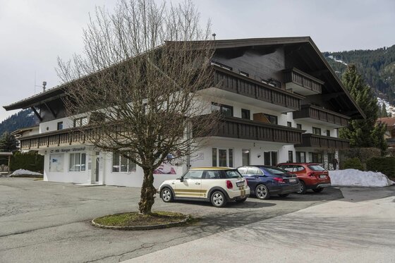 Appartement Hornblick in Reith Mehrstöckiges Gebäude im alpinen Stil mit Holzbalkonen und davor parkenden Autos.