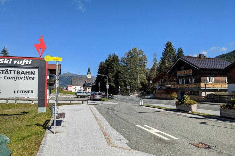 Wagstättbahn Bushaltestelle Bushaltestelle an einer Straße mit Schildern der Wagstättbahn und Blick auf eine Kirche im Hintergrund.