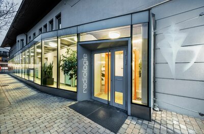 Eingangsbereich einer radiologischen Praxis mit Glasfront und grauer Tür.