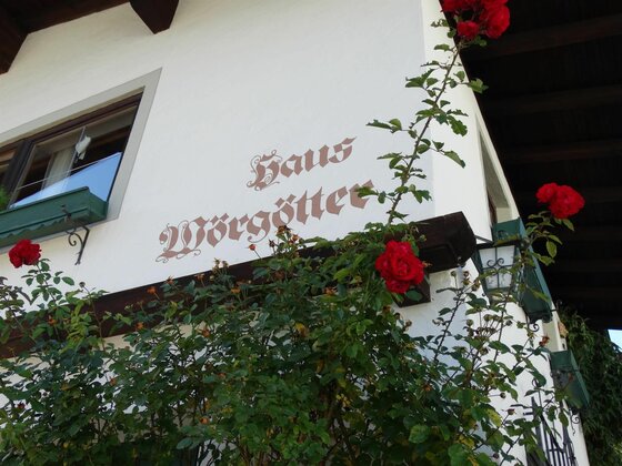 Weiße Hausfassade mit dem Schriftzug Haus Wörgötter und roten Rosen im Vordergrund.