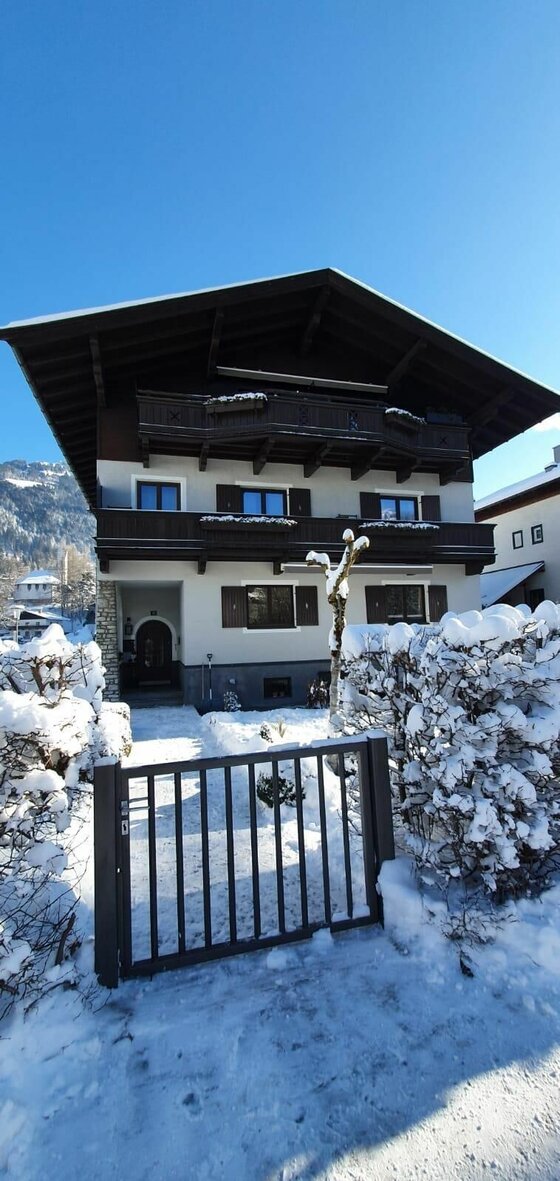 Haus Pankratz im Winter Mehrstöckiges alpines Wohnhaus mit Holzbalkonen im Winter vor blauem Himmel.