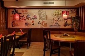 Innenansicht eines China-Restaurants mit runden Holztischen und einer großen Wandmalerei mit asiatischen Motiven.