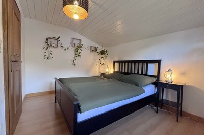 Schlafzimmer mit dunklem Doppelbett, grüner Bettwäsche, Nachttischen und Wandpflanzen unter einer Dachschräge.