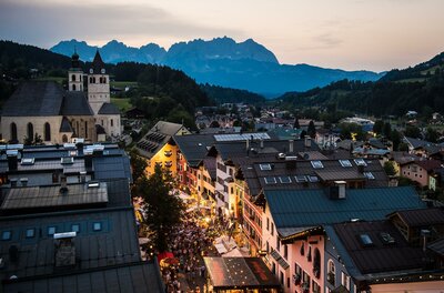 Blick über die Dächer von Kitzbühel mit Kirche und Gebirgskette im Hintergrund während der Dämmerung.