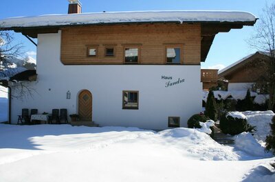 Haus Sandra im Winter Zweistöckiges Haus mit weißer Fassade, Holzobergeschoss und schneebedecktem Dach in einer Winterlandschaft.