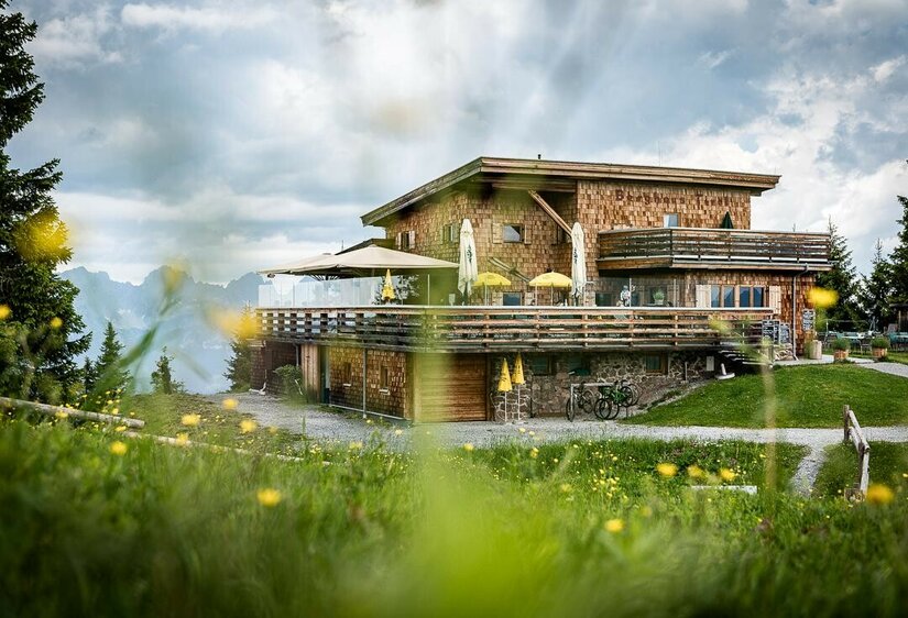 Modernes Berghaus aus Holz mit großer Terrasse vor Gebirgspanorama.