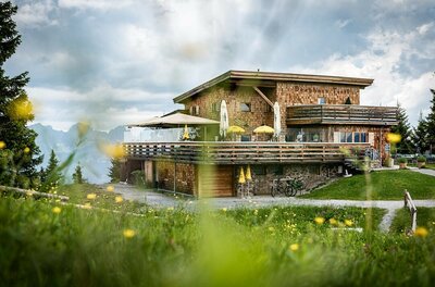 Modernes Berghaus aus Holz mit großer Terrasse vor Gebirgspanorama.