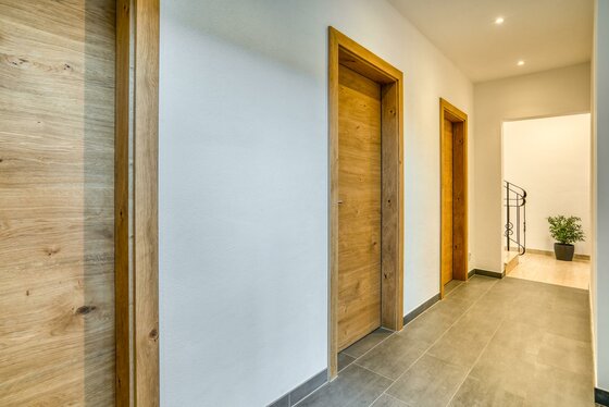 Moderner Flur mit hellen Holztüren, grauen Bodenfliesen und weißer Wand.