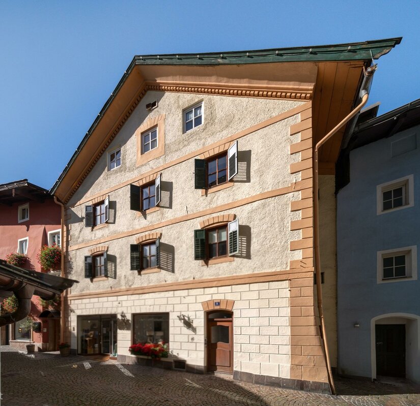 Hausansicht Hinterstadt Ein charmantes, mehrstöckiges Gebäude mit bunten Fenstern und einem traditionellen Dach. Die Fassade ist in warmen Farben gehalten und es gibt Pflanzen vor dem Eingang.