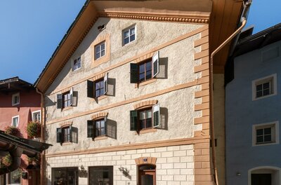 Hausansicht Hinterstadt Ein charmantes, mehrstöckiges Gebäude mit bunten Fenstern und einem traditionellen Dach. Die Fassade ist in warmen Farben gehalten und es gibt Pflanzen vor dem Eingang.