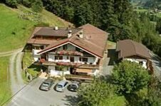 Luftaufnahme eines alpinen Gasthofs mit Parkplatz am Waldrand.