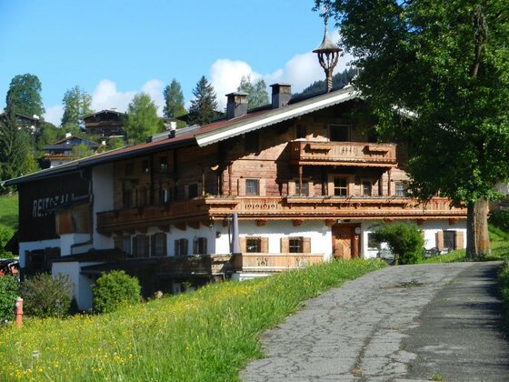 Henntalhof in Kitzbühel Traditioneller Bauernhof aus Holz und Stein mit Balkonen vor einer grünen Wiese.
