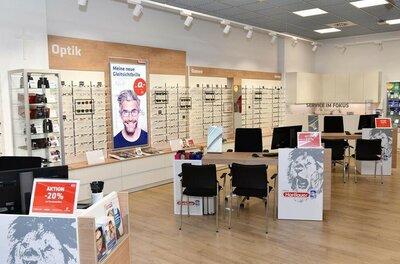 Innenansicht eines Hartlauer Optik-Fachgeschäfts mit Brillenregalen und Beratungstischen.
