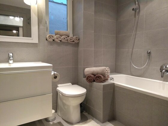 Badezimmer der Kitzbüheler Suite Modernes Badezimmer mit Badewanne, Toilette, Waschbecken und grauen Fliesen.