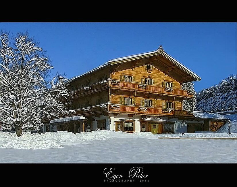 Ein mehrstöckiges Holzgebäude im alpinen Stil in einer verschneiten Winterlandschaft unter blauem Himmel.