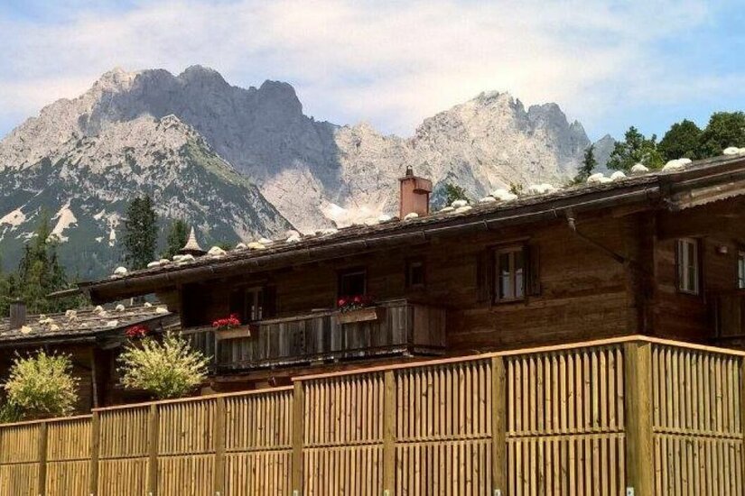 Holzhaus vor Bergpanorama Rustikales Holzhaus mit Schindeldach vor einer markanten Felskulisse der Alpen.