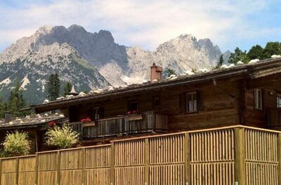 Rustikales Holzhaus mit Schindeldach vor einer markanten Felskulisse der Alpen.