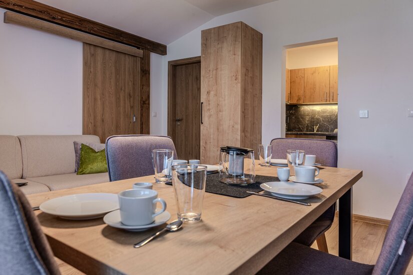 Gedeckter Holztisch mit Geschirr und Gläsern in einem modern eingerichteten Apartment.