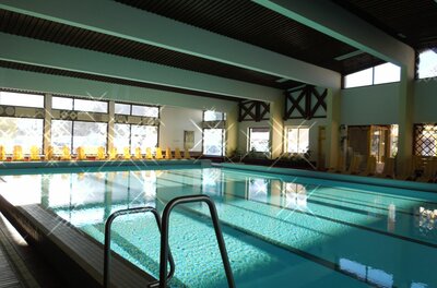 Aubad Fieberbrunn Ein Schwimmbad mit klarem Wasser und einem modernen, hellen Innenraum. Große Fenster sorgen für viel Tageslicht und eine einladende Atmosphäre.