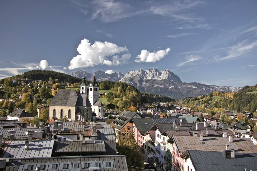 Stadführungen Eine malerische Stadtkulisse mit traditionellen Gebäuden und einer Kirche im Vordergrund. Im Hintergrund erheben sich majestätische Berge unter einem klaren Himmel.