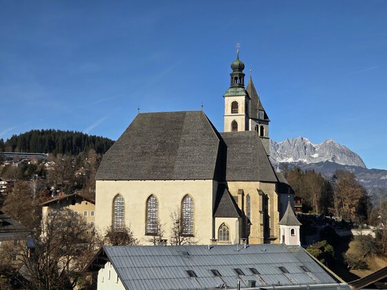 Blick St. Andreas Kirche Eine beeindruckende Kirche mit einem markanten Turm in einer malerischen Landschaft. Im Hintergrund sind Berge und ein klarer Himmel zu sehen.