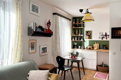 Ein gemütliches Wohnzimmer mit einer kleinen Essecke und einer Küche im Hintergrund. Helle Farben und eine einladende Atmosphäre prägen den Raum.