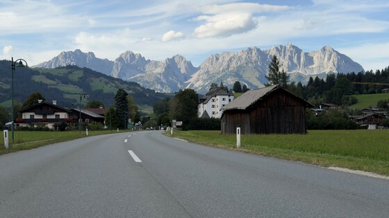 Blick auf den Wilden Kaiser Asphaltierte Landstraße führt auf ein Bergmassiv mit schroffen Felsgipfeln zu.