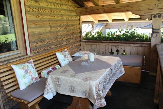 Balkon im Haus Kreidl Überdachter Holzbalkon mit Sitzbank, Kissen und gedecktem Tisch.