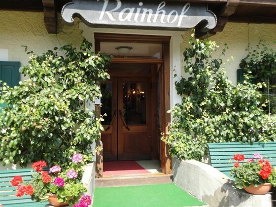 Hölzerner Eingangsbereich der Pension Rainhof mit Blumenkästen und grünen Bänken.