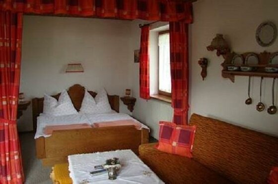 Rustikales Schlafzimmer mit Doppelbett aus Holz, roten Vorhängen und einem Sofa im Vordergrund.