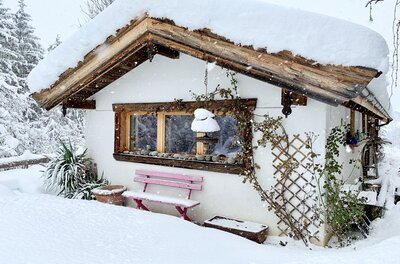 Verschneite Hütte mit rosa Holzbank und schneebedecktem Dach bei leichtem Schneefall.
