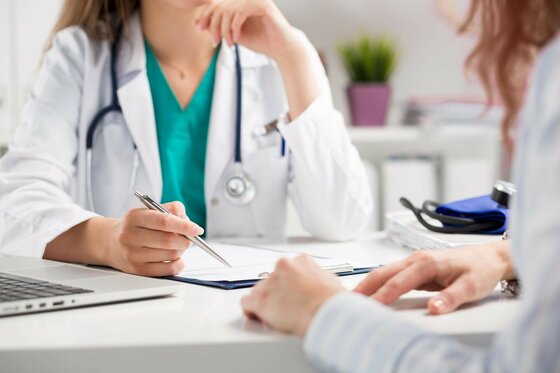 Medizinische Beratung bei Medkitz.plus Ärztin im weißen Kittel mit Stethoskop führt ein Beratungsgespräch mit einer Patientin an einem Schreibtisch.