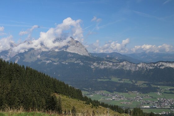 Aussicht vom Harschbichl Blick vom Harschbichl auf ein bewaldetes Tal und markante Berggipfel unter leicht bewölktem Himmel.