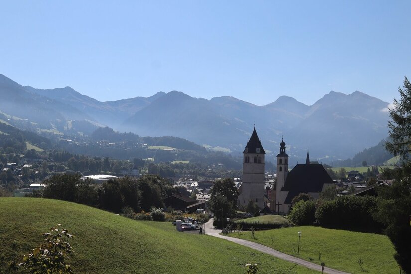 Blick auf eine Kirche mit zwei Türmen vor einer Gebirgskette unter blauem Himmel.