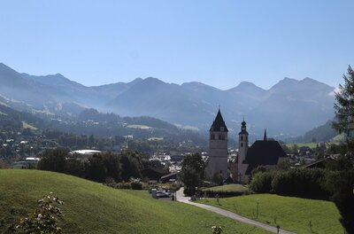 Blick auf eine Kirche mit zwei Türmen vor einer Gebirgskette unter blauem Himmel.