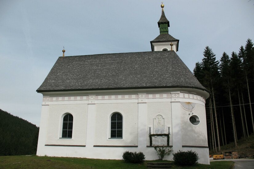 Wallfahrtskapelle Jochbergwald Eine kleine, weiße Kirche mit einem grauen Dach und einem Spitzdach-Glockenturm. Umgeben von Bäumen und einer ruhigen Landschaft.