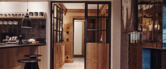 Penthouse Lodge Private Spa Moderner Innenraum mit Holzwänden, einer Glastür mit schwarzem Rahmen und einer Bar mit Hockern.