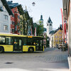Ein gelber Bus fährt durch die malerische Innenstadt von Kitzbühel, umgeben von bunten Gebäuden und einem klaren Himmel.